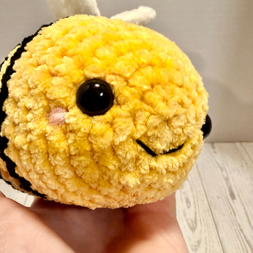 Plush bee toy held in a hand against a neutral background